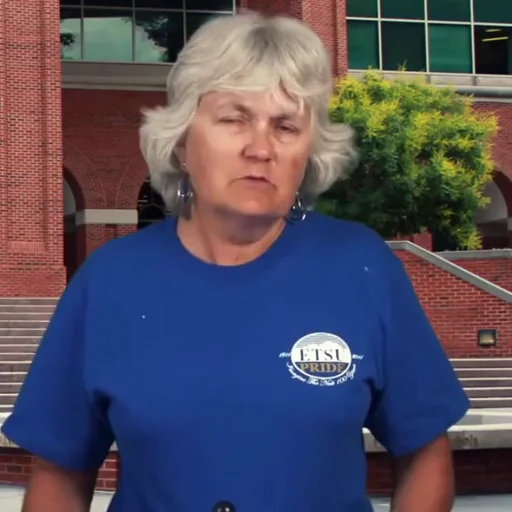 Source talking video: speaker outdoors in front of a brick building